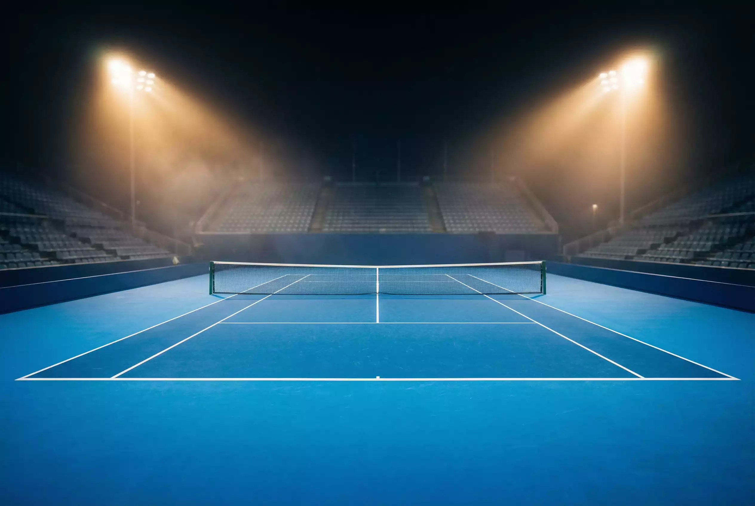 Pista de tenis profesional iluminada durante un partido nocturno con líneas de saque visibles